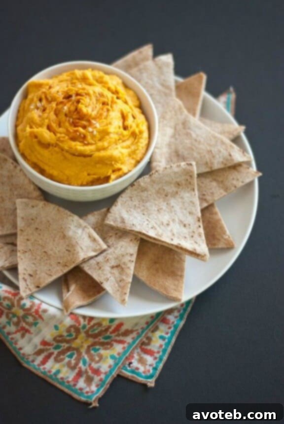 15 Recipes for Creamy Dreamy Hummus Bliss 14 A warm, inviting orange-hued Spicy Sweet Potato Hummus, garnished with vibrant chili flakes, a sprig of fresh cilantro, and a drizzle of olive oil. This dip is both comforting and zesty, perfect for cooler months.