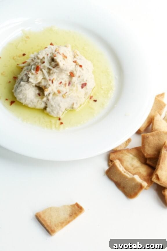 15 Recipes for Creamy Dreamy Hummus Bliss 15 A rustic bowl of Italian White Bean Hummus, elegantly garnished with fresh basil leaves, a sprinkle of red pepper flakes, and a delicate drizzle of olive oil. This Mediterranean-inspired dip offers a creamy texture and herbaceous flavor.