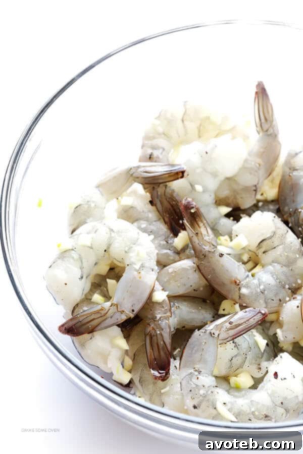 Raw shrimp being tossed with minced garlic and white wine in a mixing bowl.