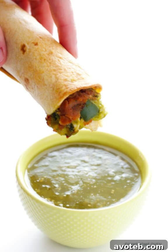 Close-up of a chicken guacamole taquito being dipped in salsa