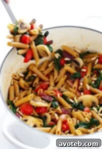 Top-down view of a serving of pasta with mushrooms, tomatoes, and spinach on a white plate.