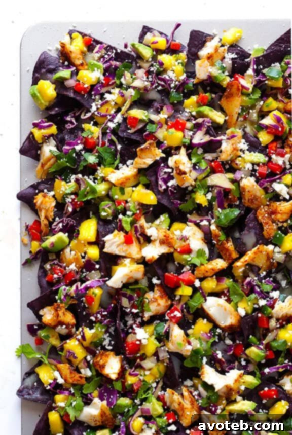 The fully assembled Rainbow Fish Taco Nachos, artfully topped with seasoned fish, fresh mango slaw, crumbled cheese, and green cilantro, ready to be served.
