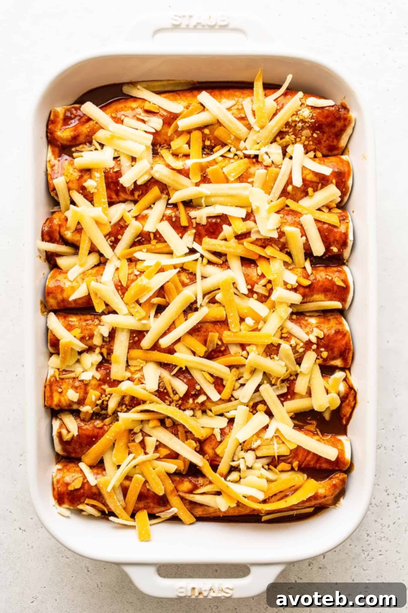 Uncooked beef enchiladas in pan with cheese