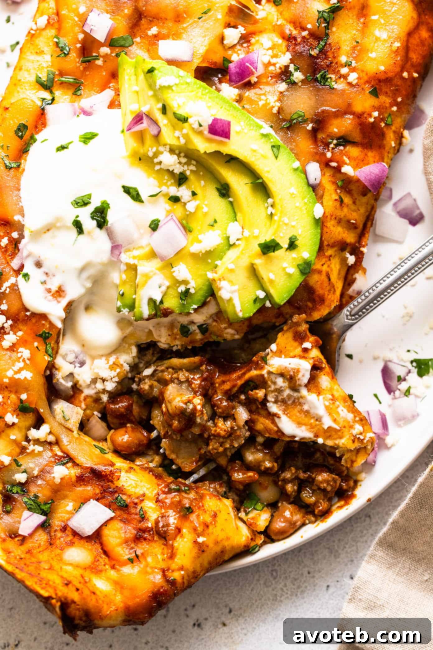 Beef enchilada closeup with avocado and sour cream