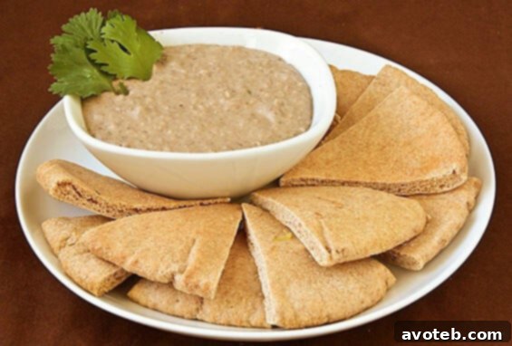 Creamy Black Bean Hummus garnished with fresh cilantro, served in a rustic bowl with colorful dippers like carrots and pita bread.
