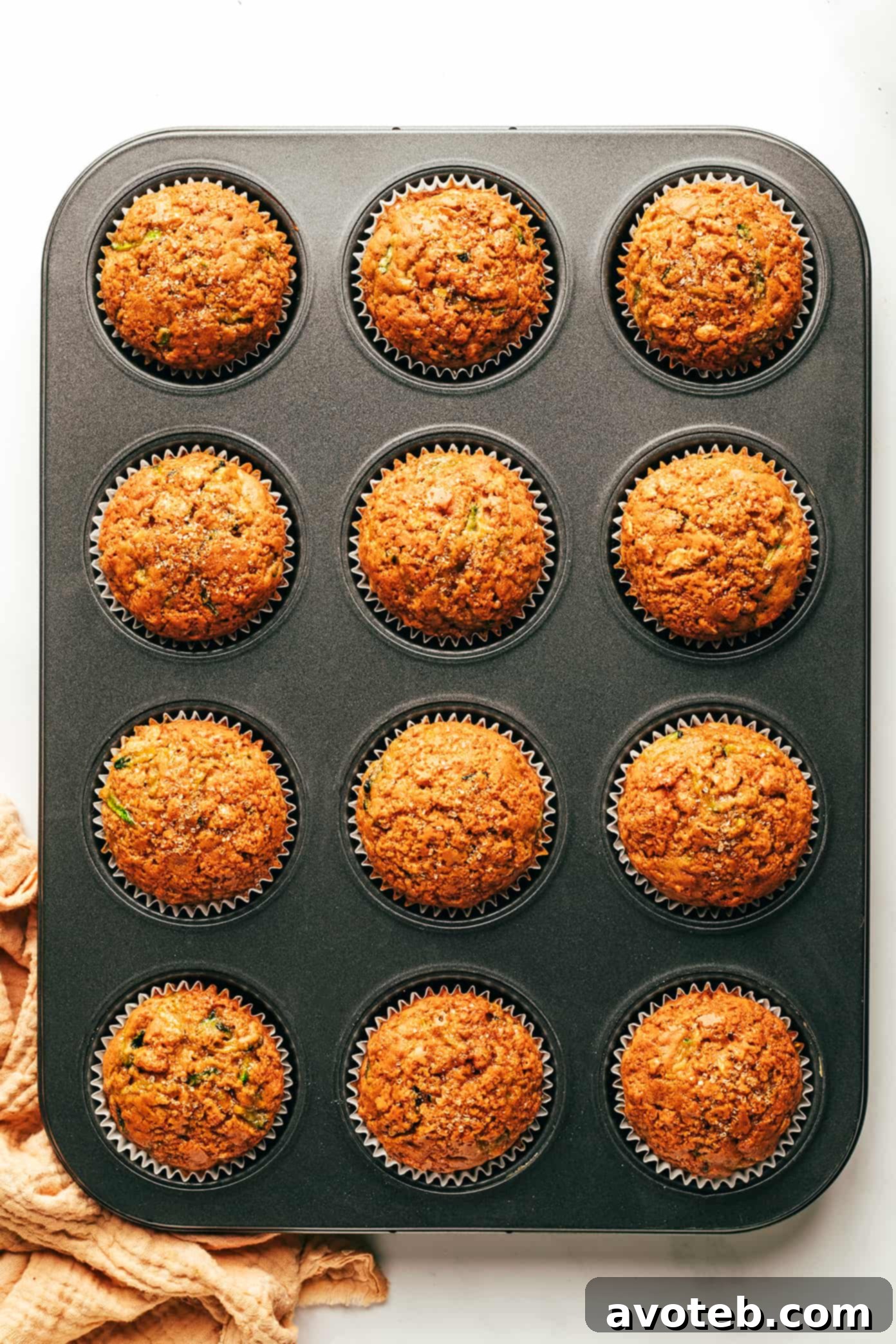 Overhead view of several healthy zucchini muffins, some with turbinado sugar sprinkling, next to fresh zucchini.