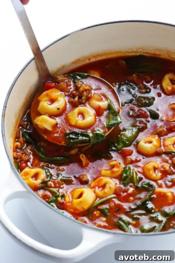 A large pot of Tortellini Soup simmering on the stove, with Italian sausage, spinach, and tomatoes visible. | gimmesomeoven.com
