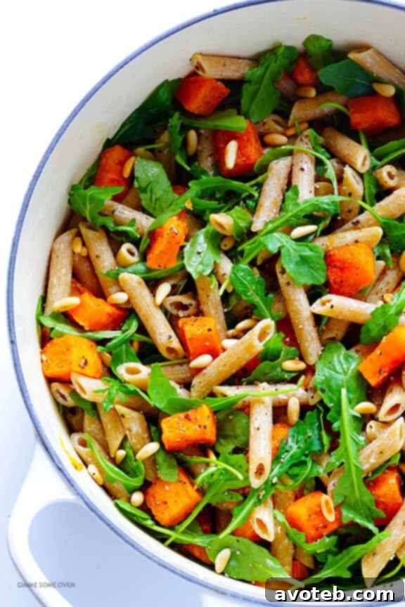 5-Ingredient Butternut Squash Pasta with Arugula and Goat Cheese 7 A vibrant bowl of freshly tossed butternut squash, arugula, and goat cheese pasta, with a fork ready to serve