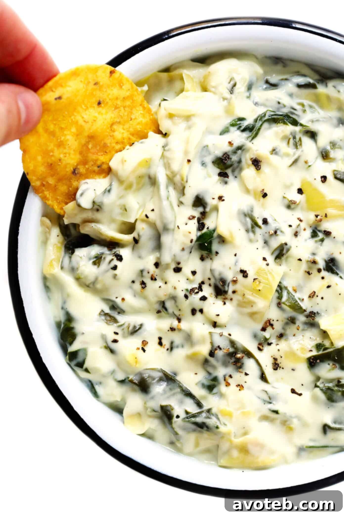 Spinach and Artichoke Dip Ready for Any Party A serving of Spinach and Artichoke Dip in a ceramic bowl with various dippers like bread and chips
