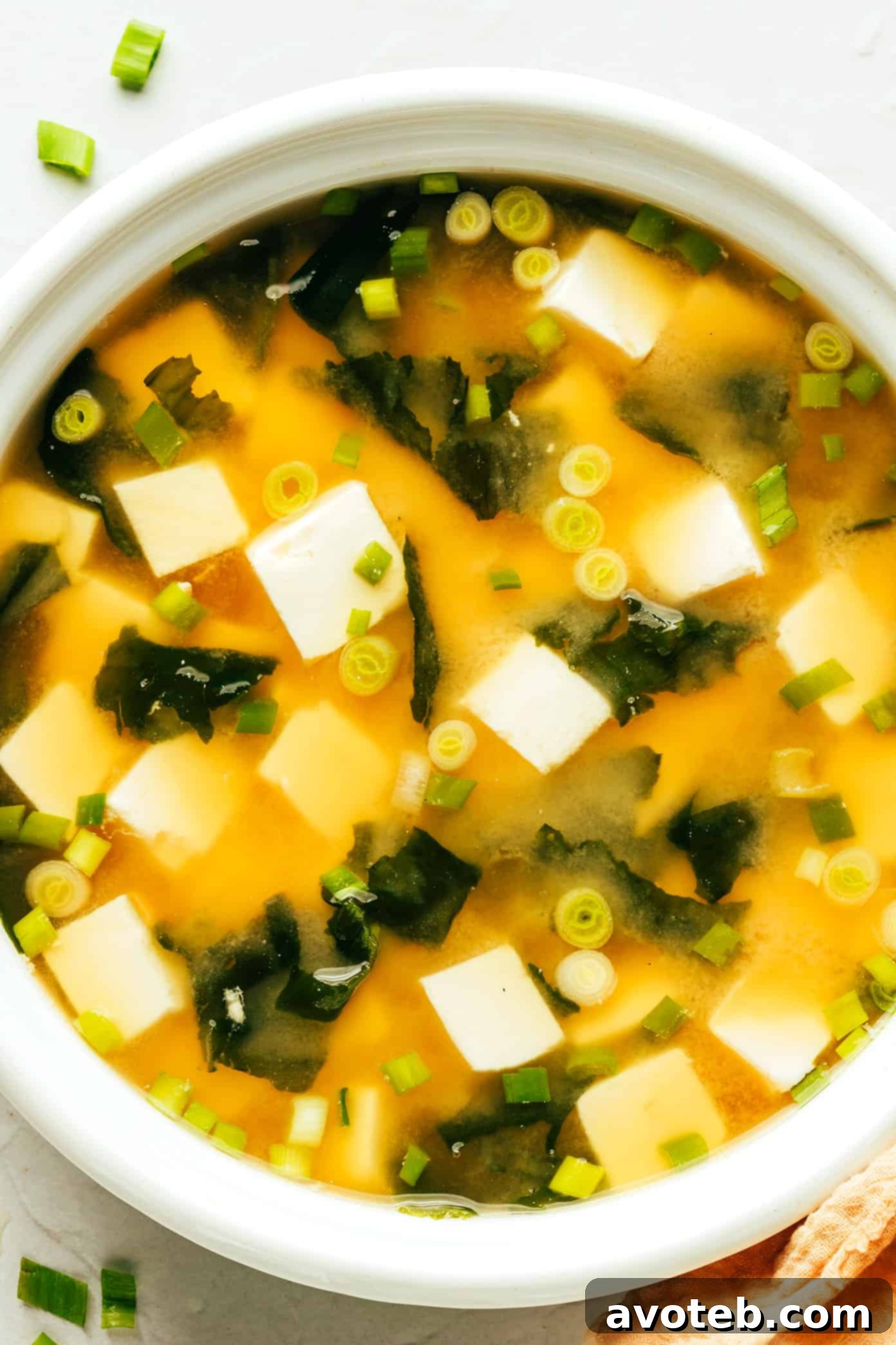 A rustic bowl filled with steaming miso soup, garnished with vibrant green scallions and delicate tofu cubes.