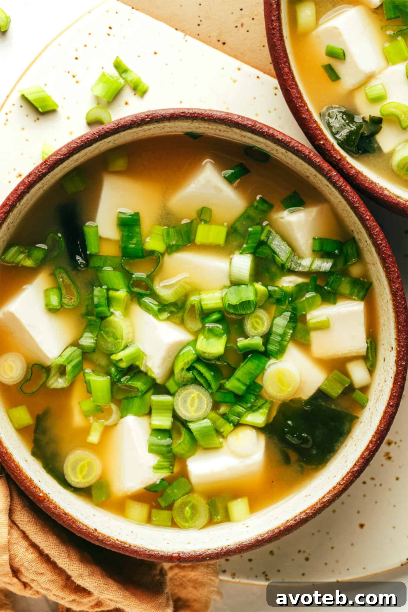 A vibrant bowl of homemade miso soup, brimming with soft tofu cubes, rehydrated wakame, and fresh green scallions.