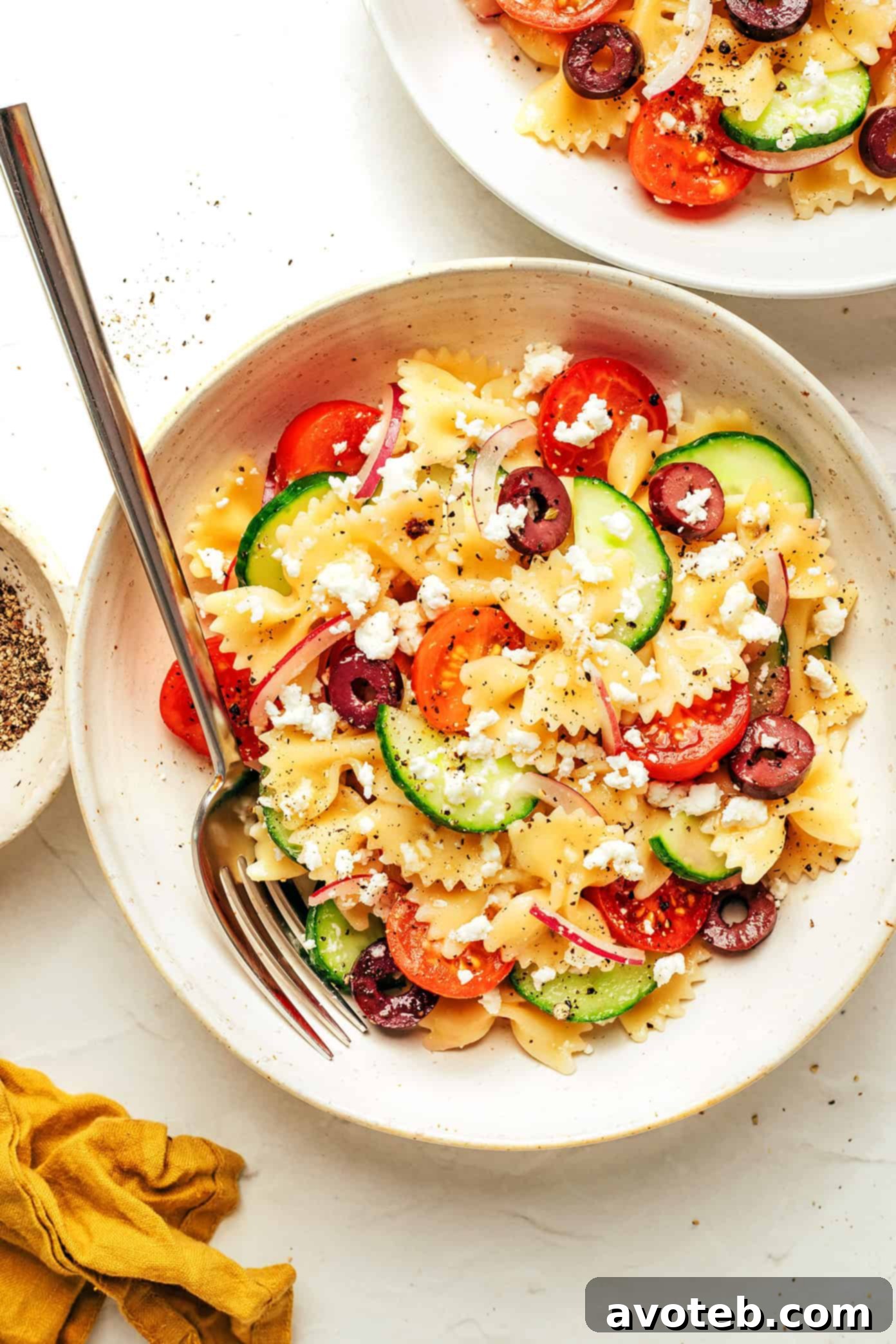 Overhead shot of Mediterranean Pasta Salad in a bowl with ingredients scattered around