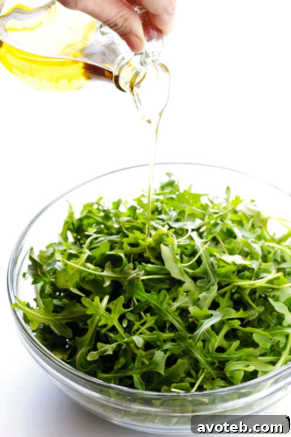 Hands preparing the 5-Ingredient Arugula Salad, demonstrating the simple steps of drizzling olive oil and lemon juice onto fresh arugula. | gimmesomeoven.com