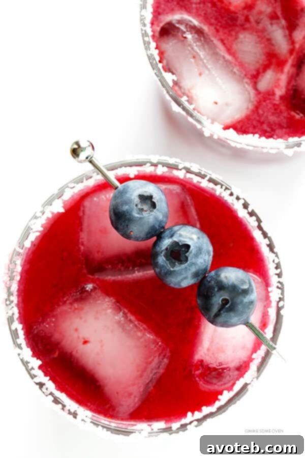 Two perfectly prepared blueberry margaritas in salt-rimmed glasses, garnished with lime and berries, on a festive table.