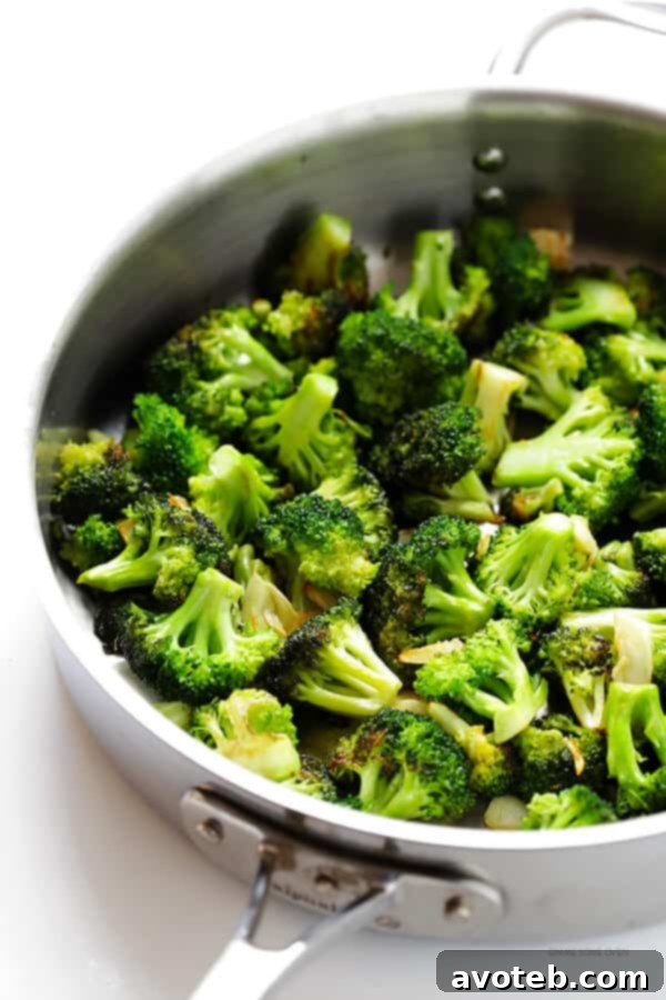 A close-up of perfectly sautéed broccoli florets with thinly sliced garlic, showing a tender-crisp texture and slight char, ready to be integrated into the sesame noodles.
