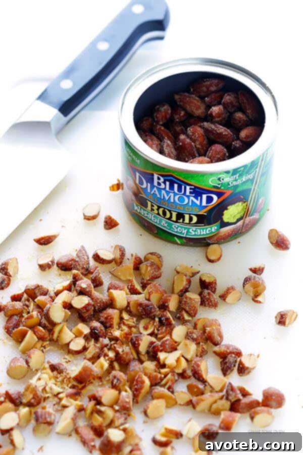 A close-up image of a hand chopping Blue Diamond Wasabi and Soy Sauce Almonds on a cutting board, emphasizing their crunchy texture and preparing them for the noodle dish.