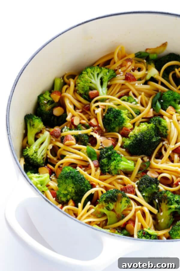 A beautifully presented bowl of colorful Sesame Noodles, garnished with fresh green onions, toasted sesame seeds, and crushed red pepper flakes, showcasing the vibrant sauce and ingredients.