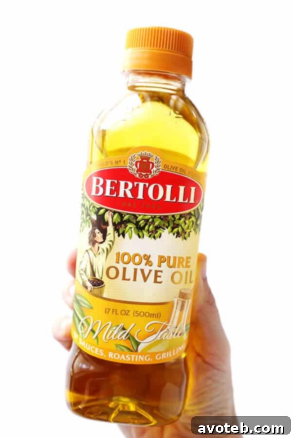 A bottle of Bertolli Pure Olive Oil beside a bowl of vibrant, colorful vegetables, highlighting healthy grilling ingredients.