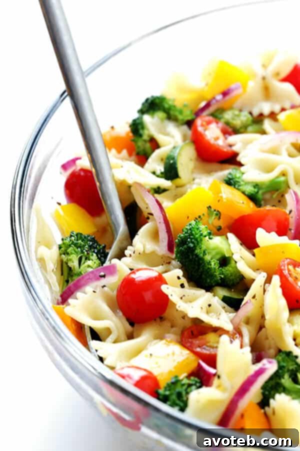 Tossing cooked pasta and sautéed vegetables with a homemade white balsamic vinaigrette in a large bowl, ensuring every piece is coated.