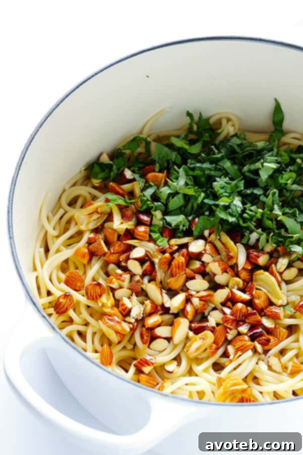 Preparation step: The aromatic mixture of sautéed garlic, lemon juice, and toasted almonds being gently stirred together, creating the flavorful base for the spaghetti.