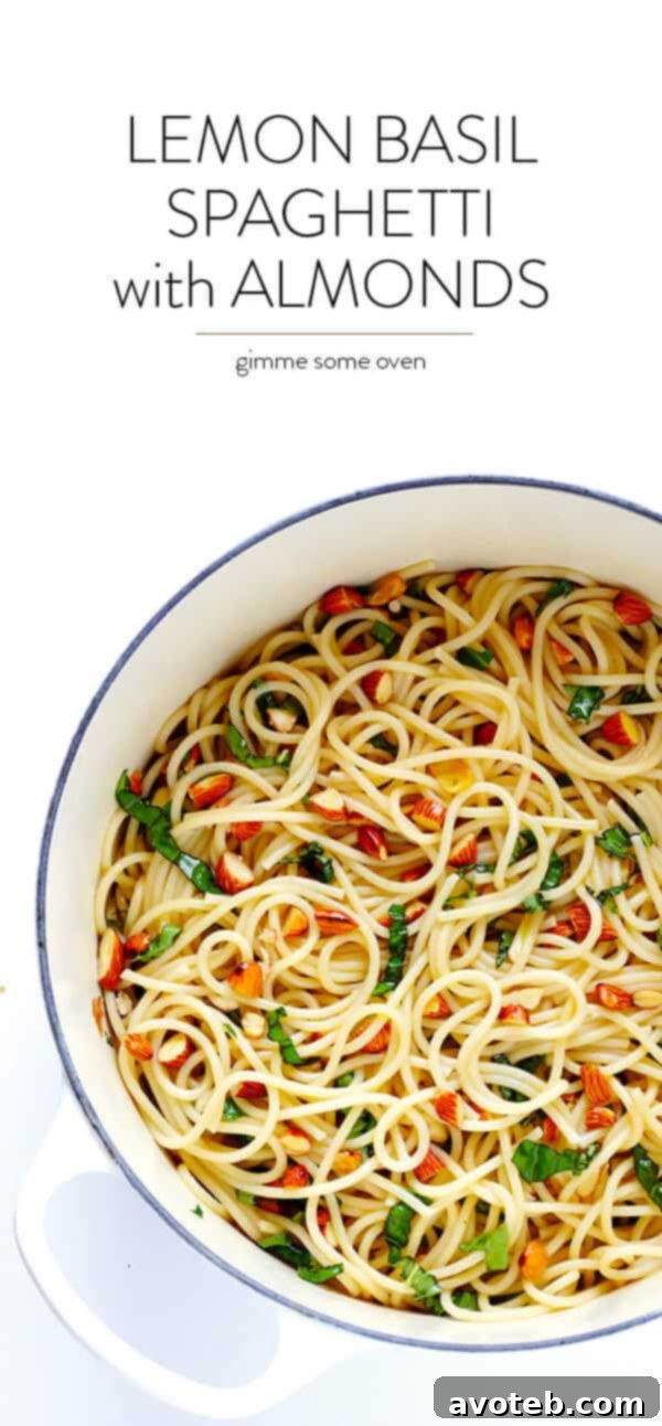 Overhead shot of a large serving bowl filled with Lemon Basil Spaghetti with Almonds, ready to be dished out. It's garnished with fresh basil leaves and grated Parmesan cheese.