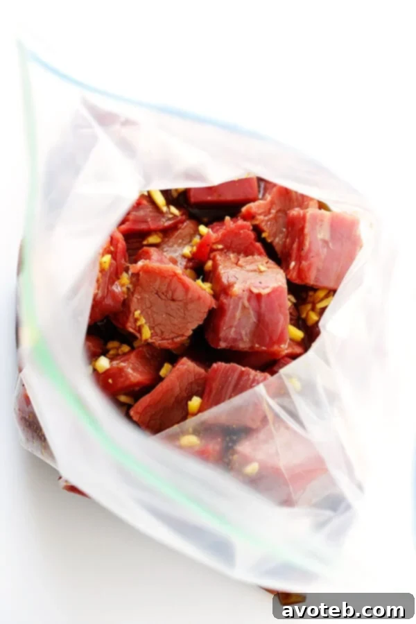 Hands tossing flank steak pieces with a rich Korean marinade in a bowl, preparing for skewering.