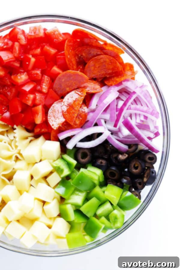 A large bowl of uncooked pasta, diced mozzarella, and fresh tomatoes, ready for pizza toppings and vinaigrette