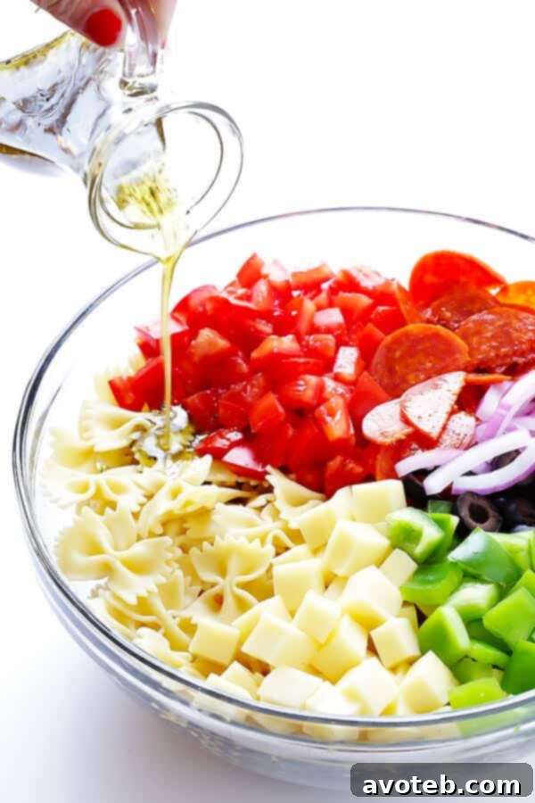Pouring a vibrant, homemade Italian vinaigrette over a bowl of fresh Pizza Pasta Salad ingredients