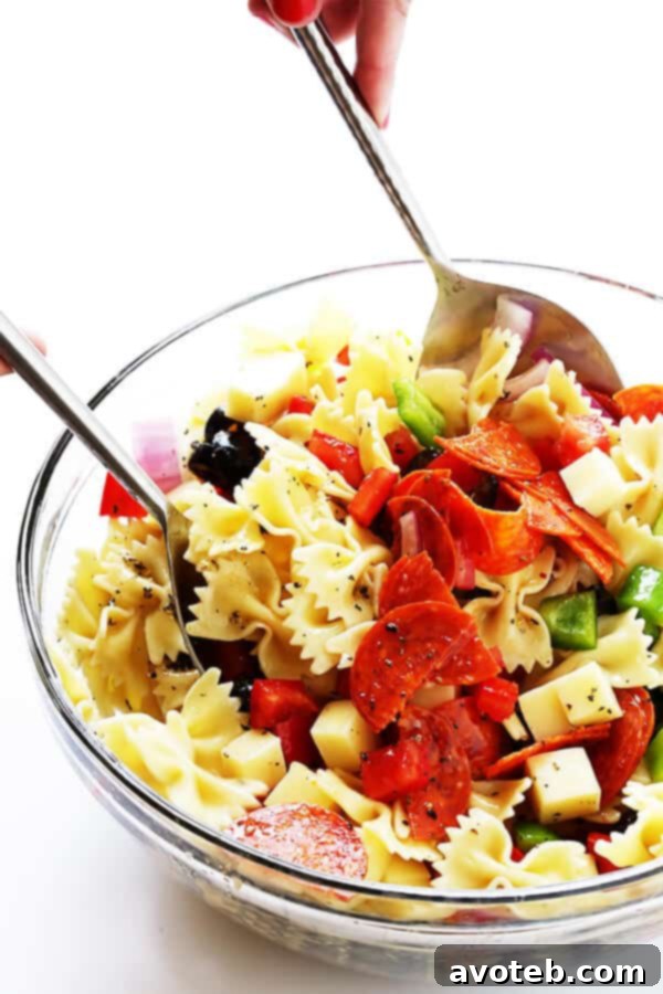Hands tossing a colorful Pizza Pasta Salad in a large mixing bowl, coated in vinaigrette