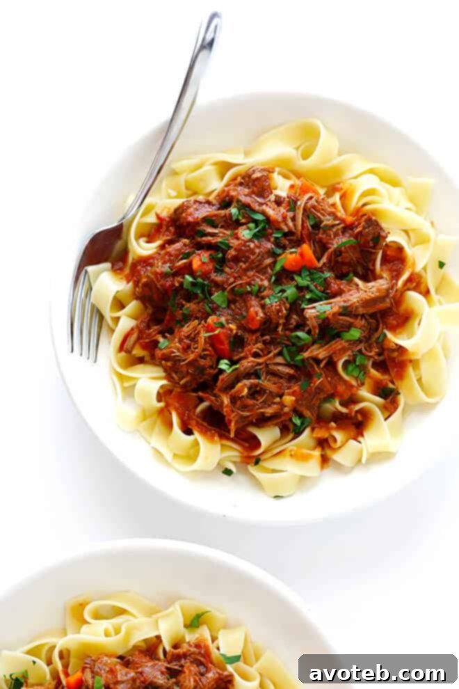 A delightful bowl of Slow Cooker Beef Ragu with pasta, topped with fresh Parmesan and parsley, ready to be savored.