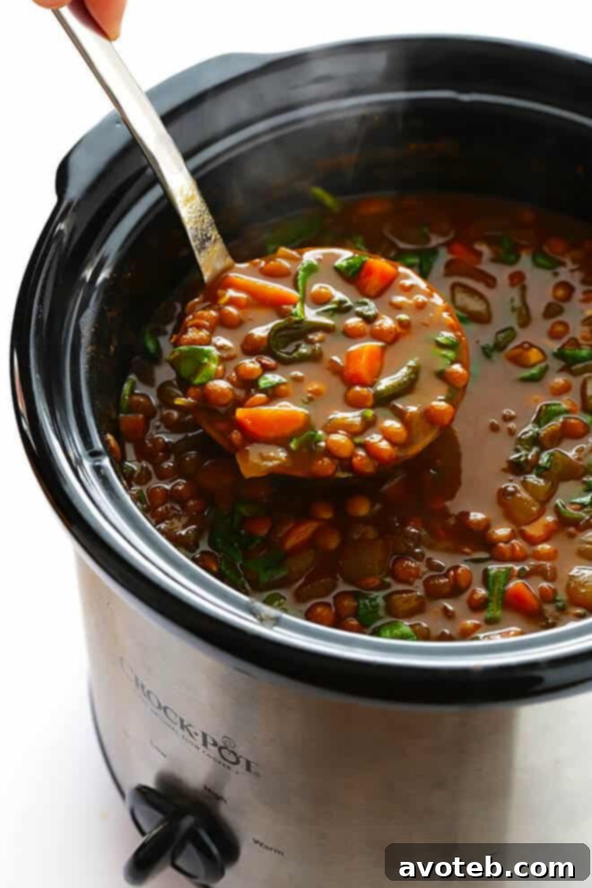 Adding fresh spinach to the Slow Cooker Curried Lentil Soup at the end of the cooking process, ensuring vibrant color and added nutrition to this healthy vegetarian recipe. | gimmesomeoven.com