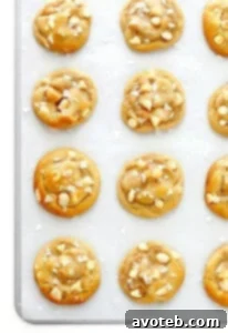 A plate of freshly baked Salted White Chocolate Macadamia Nut Cookies, glistening with sea salt flakes.