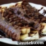 Stacked chocolate banana crepes with melted chocolate and banana slices.