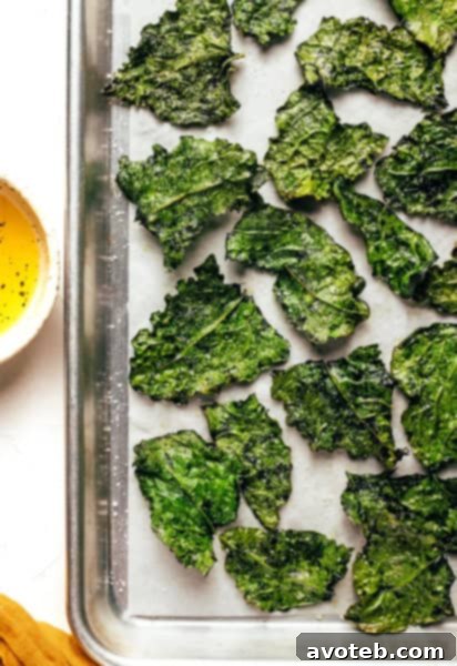 A large batch of golden, crispy kale chips piled high on a white serving plate.