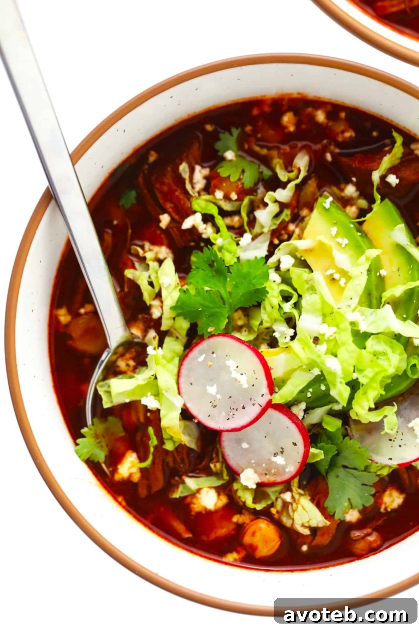 Topped Pork Pozole Bowl A beautifully garnished bowl of pork pozole with fresh avocado slices, thinly sliced radishes, a sprinkle of cilantro, and shredded cabbage, ready to be enjoyed.