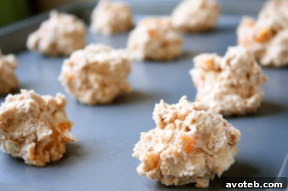Oatmeal Apricot White Chocolate Cookie Dough Scoops Close-up of oatmeal cookie dough being scooped onto a baking sheet, showing generous amounts of apricots and white chocolate