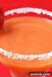 A close-up of a Strawberry Mango Margarita in a glass with a lime wedge and fresh berries.