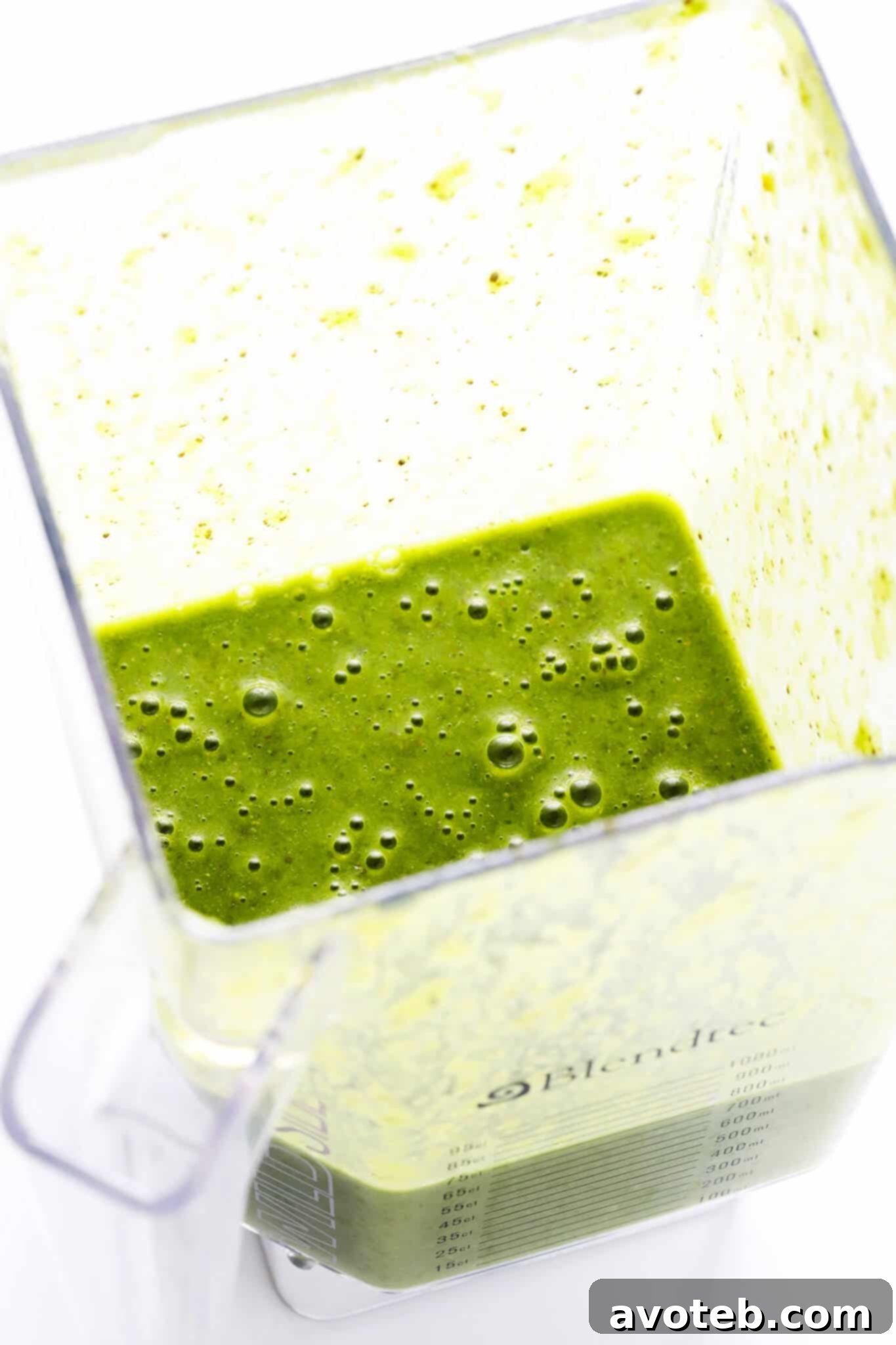 A blender filled with green smoothie ingredients, mid-blend, showing the swirling green mixture.