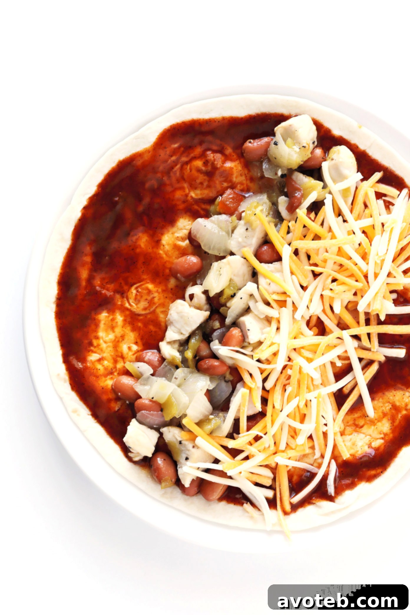 A pan of Ancho Chicken Enchiladas, generously topped with sauce and shredded cheese, ready to be baked to bubbly perfection. A hearty and satisfying meal.