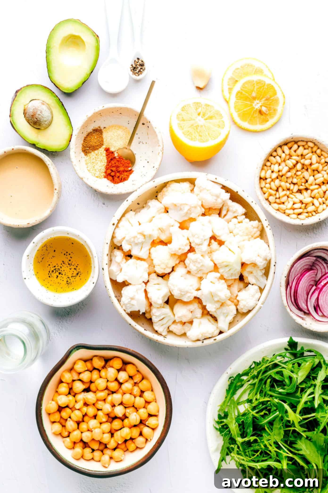 A vibrant and fresh Roasted Cauliflower, Chickpea, and Arugula Salad in a large white bowl, garnished with herbs and a side of dressing.