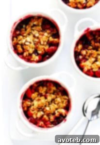 Delicious Cranberry Crisp in a small white ramekin, topped with vanilla ice cream, on a wooden board with fresh cranberries.