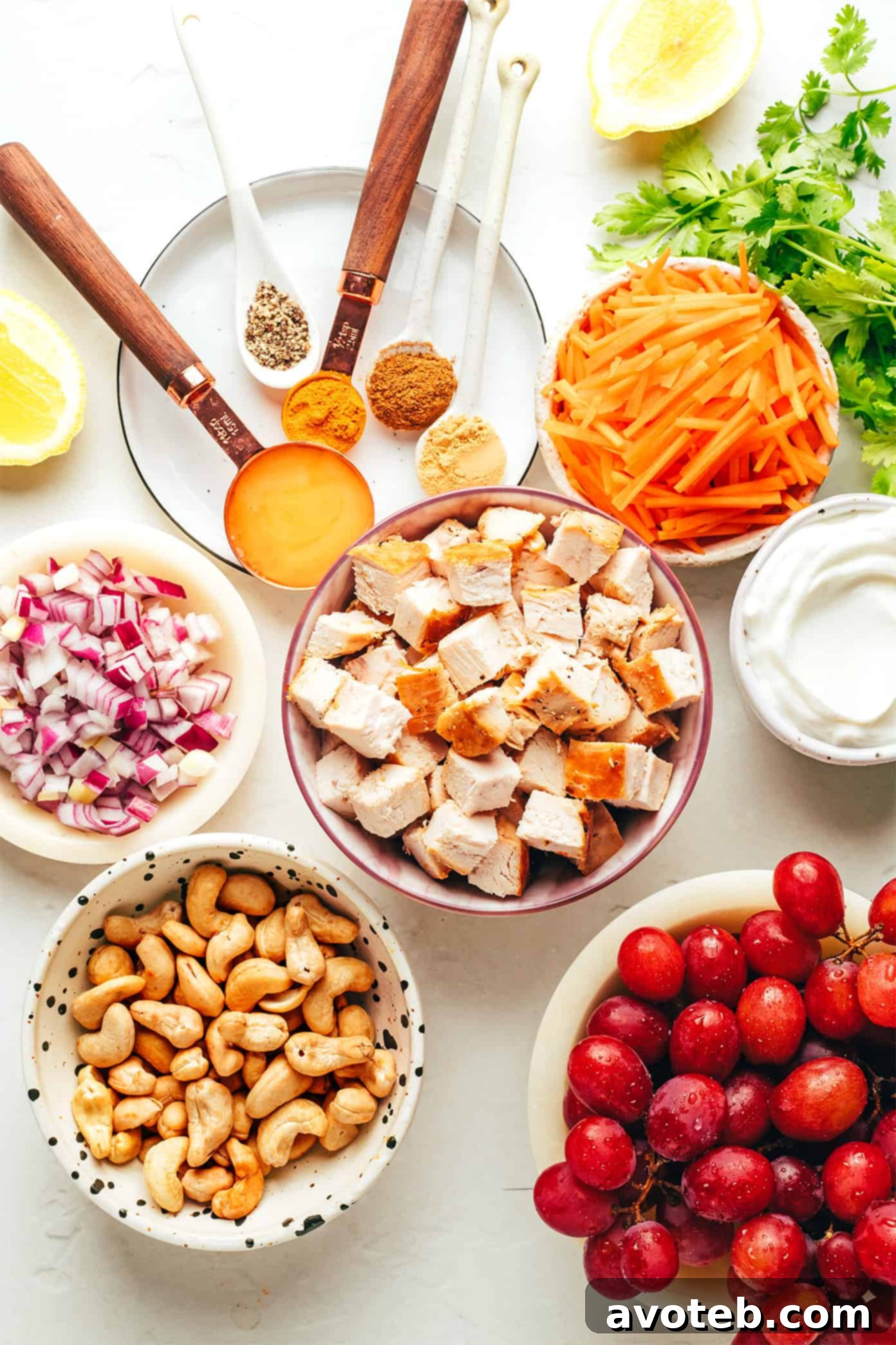 Ingredients laid out for a healthy curry chicken salad, including cooked chicken, grapes, carrots, cashews, red onions, and various spices.