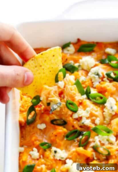 Close up of a spoonful of creamy Buffalo Cauliflower Dip being scooped from a white serving dish.