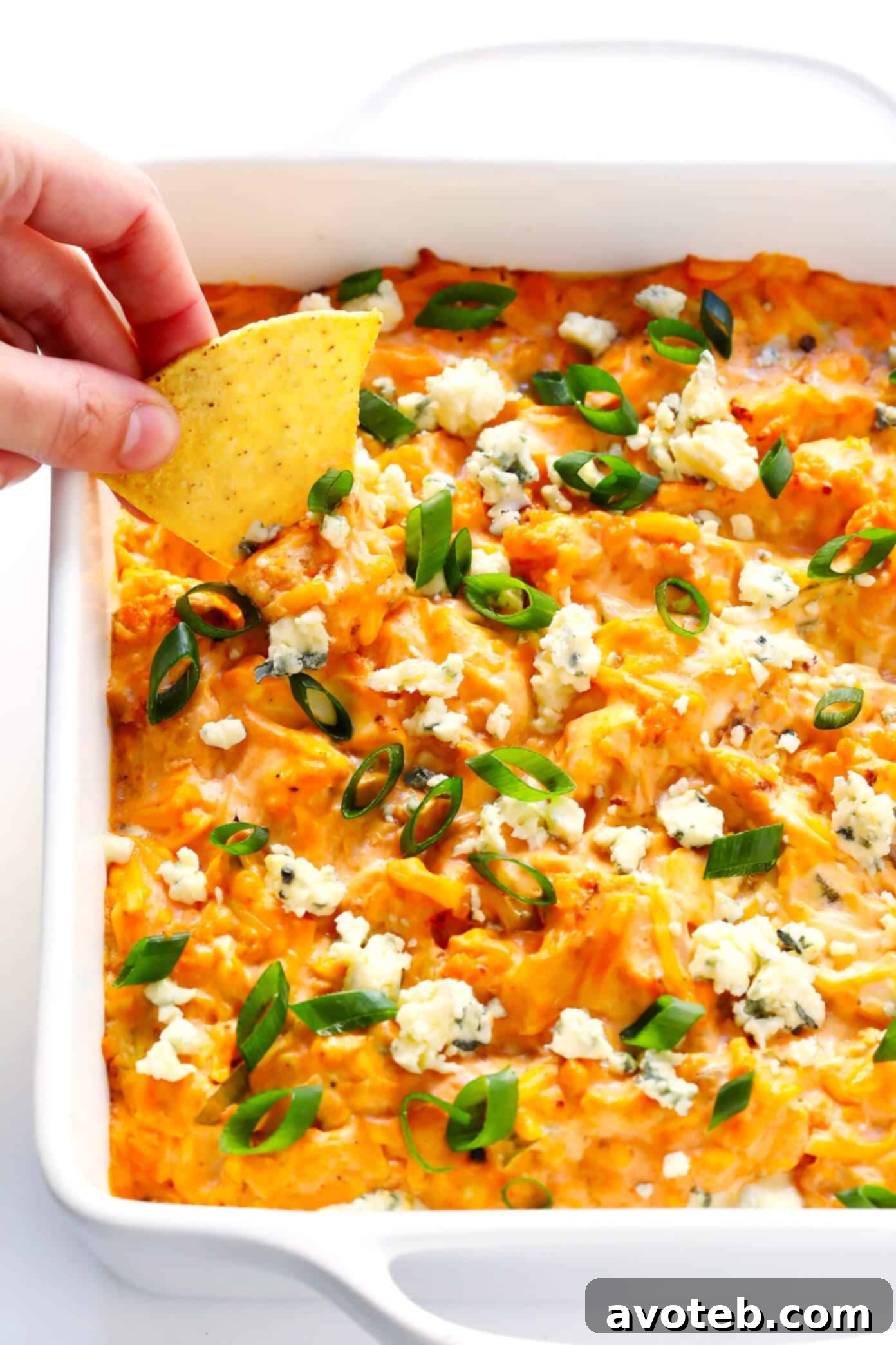 A close-up shot of a freshly baked Buffalo Cauliflower Dip, topped with blue cheese and green onions, ready for scooping.