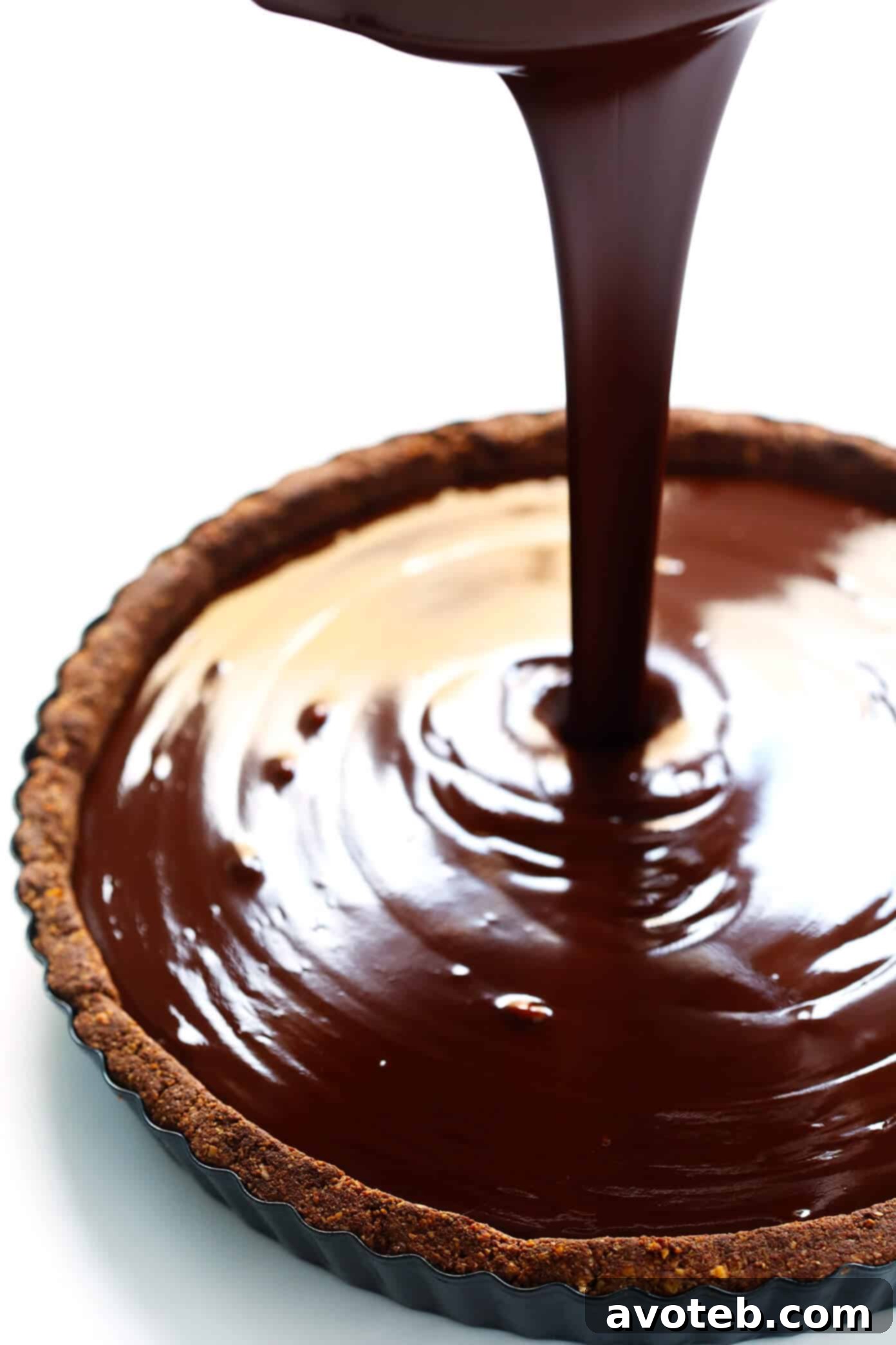 Smooth dark chocolate filling being carefully poured into a baked, golden-brown tart crust set in a tart pan.