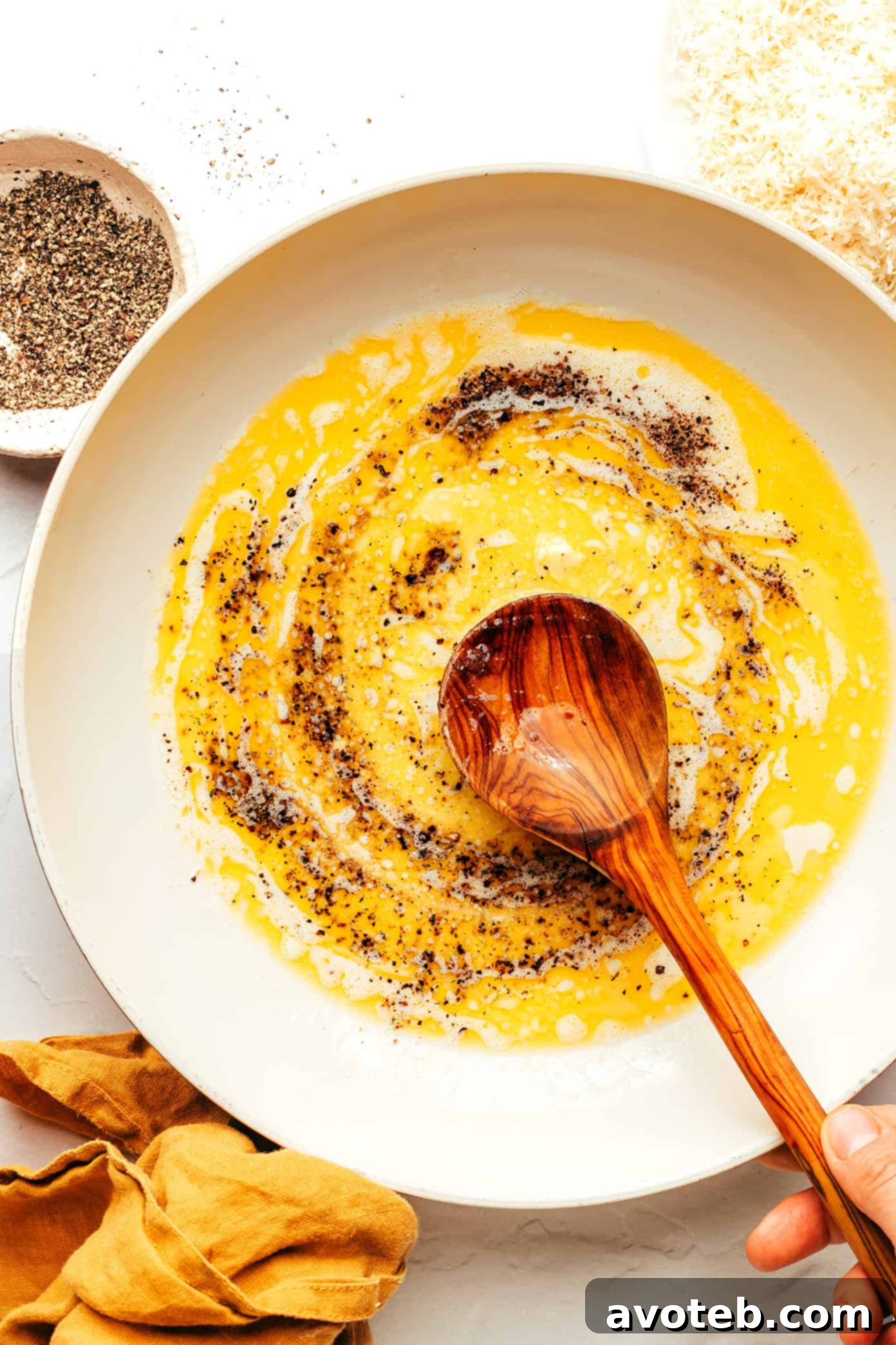 Chef's hands tossing pasta with creamy Cacio e Pepe sauce in a large sauté pan.