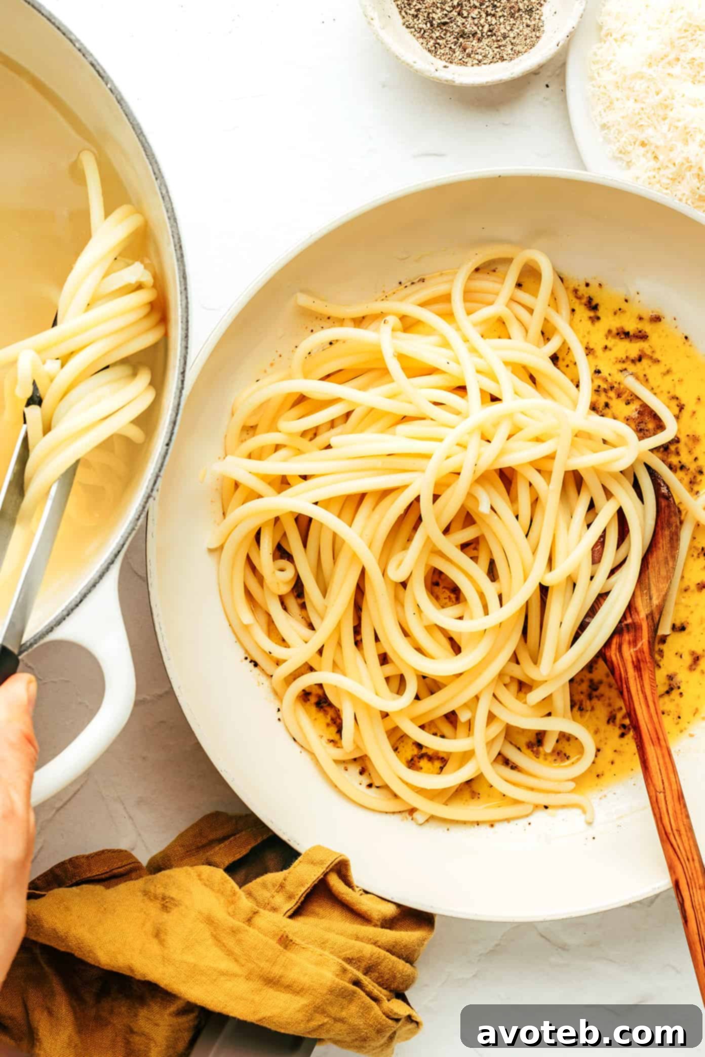 Close-up of Bucatini Cacio e Pepe being tossed in a pan, the creamy sauce coating every strand.