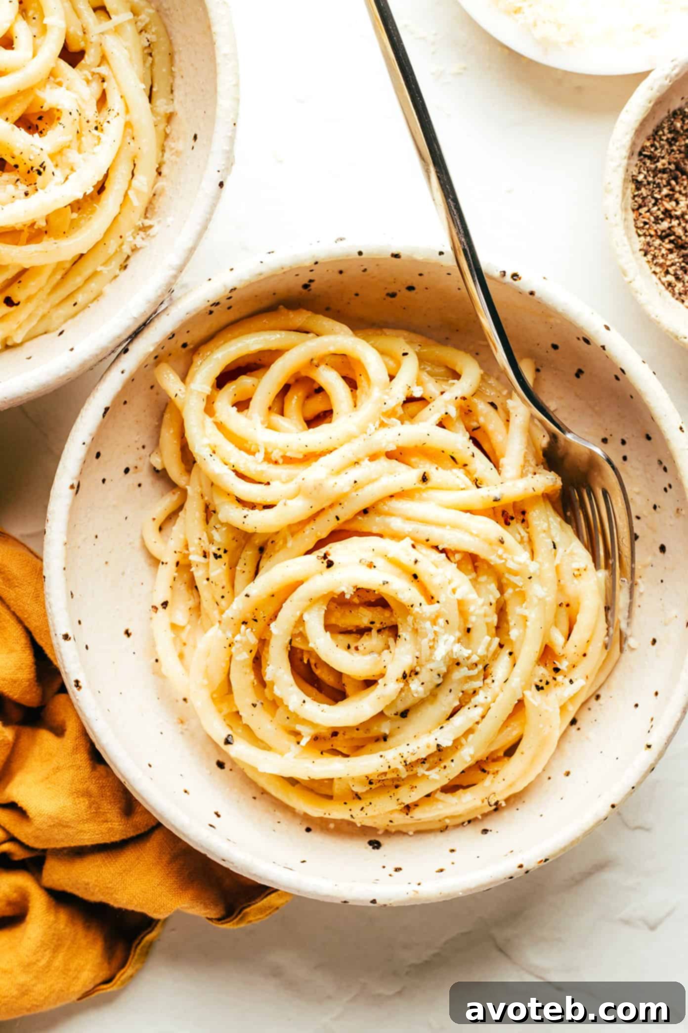 A serving bowl filled with a generous portion of creamy Bucatini Cacio e Pepe, garnished with extra grated cheese and black pepper.