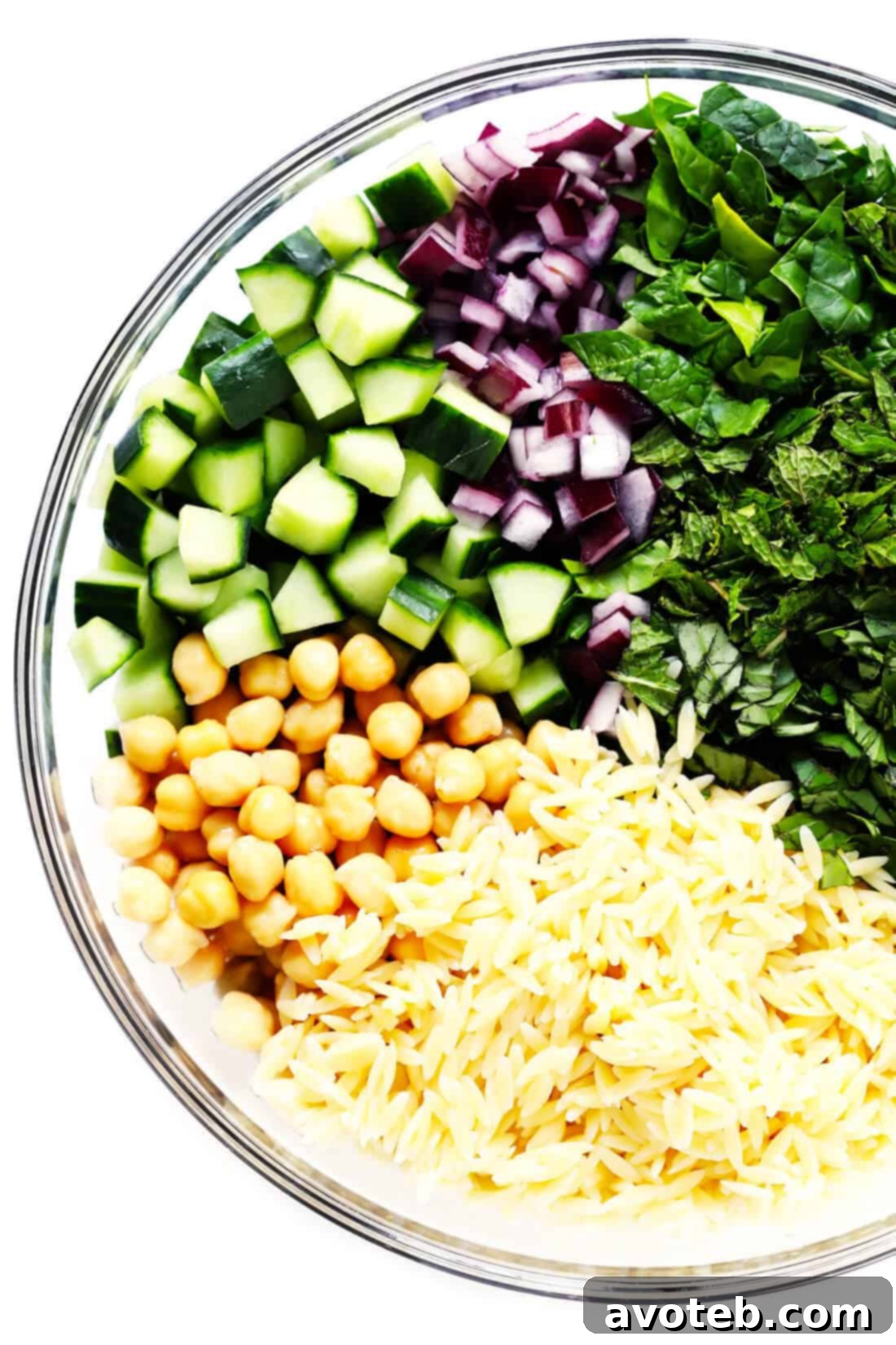 Ingredients for Lemony Orzo Pasta Salad laid out, including orzo, spinach, chickpeas, cucumber, red onion, and fresh herbs.