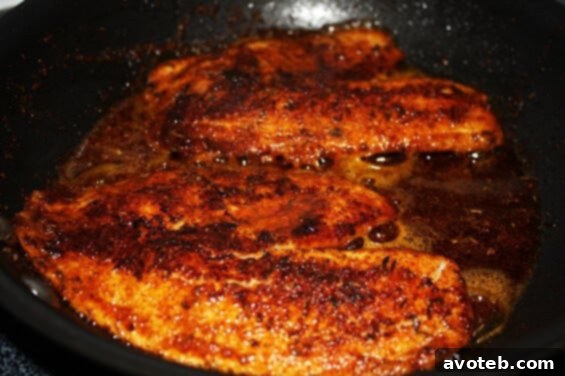 blackened tilapia cooking in a hot skillet with steam